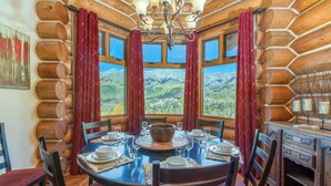 A log cabin interior with a dining table set for four, surrounded by chairs, and large windows offering a mountain view. - Townhomes On The Creek 119 (Mountain Village)
