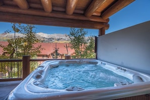 Un bain à remous surmonté d’une pergola en bois, entouré d’une terrasse en bois et offrant une vue sur les montagnes.