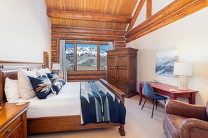 A bedroom with a wooden bed, a desk, a chair, and a view of mountains.