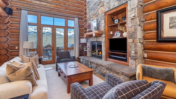 A log cabin interior with a stone fireplace, wooden furniture, and a view of mountains through large windows. - Tristant 205: Ski&Hiking Access w/Hot Tub,Views | 3BR Luxury in Mountain Village (Mountain Village)