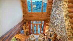 A cozy log cabin interior with a stone fireplace, wooden furniture, and a view of mountains through large windows. - Tristant 205: Ski&Hiking Access w/Hot Tub,Views | 3BR Luxury in Mountain Village (Mountain Village)