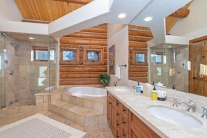 A modern bathroom with a wooden log wall, a glass shower enclosure, and a large vanity with two sinks.