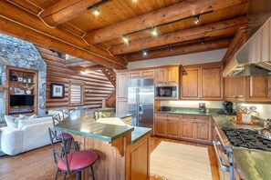 A log cabin interior with a stone fireplace, wooden cabinets, a kitchen island, and a cozy seating area.