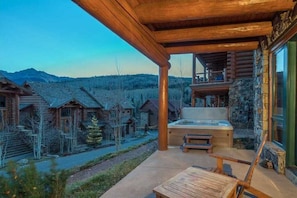 Une terrasse en bois avec un jacuzzi, offrant une vue sur un village de montagne.