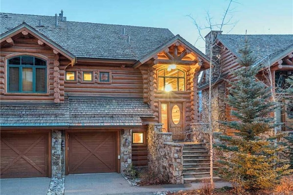 Une cabane en rondins avec des fondations en pierre, un garage en bois et un escalier menant à un porche.