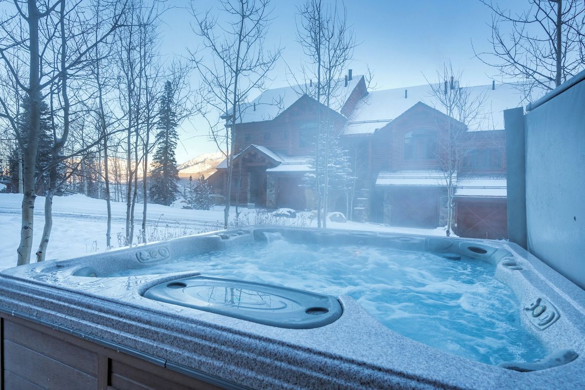 A hot tub with a snowy landscape and buildings in the background.