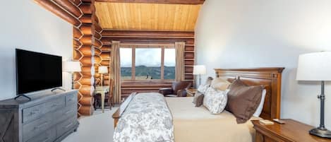 Quarto com cama grande, cabeceira de madeira, televisão e vista para as montanhas.