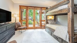 A room with a bunk bed, a television, a desk with drawers, a chair, and a large window with a view of greenery. - Spacious 4 Bedroom Villa with Ski-in Ski-out Access (Mountain Village)