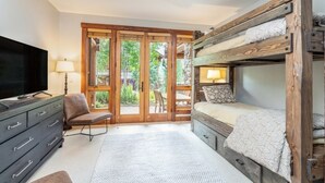A room with a bunk bed, a television, a chair, a lamp, and a view through a glass door. - Villas At Tristant 201 (Mountain Village)