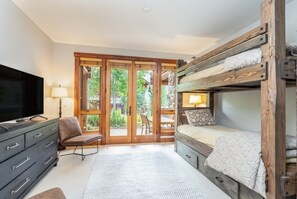 A room with a bunk bed, a television, a chair, a lamp, and a view through a glass door. - Villas At Tristant 201 (Mountain Village)