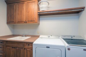 A kitchen with wooden cabinets, a sink, a washing machine, and a drying rack.