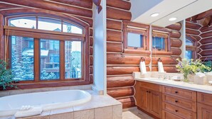 A log cabin bathroom with a large window, a bathtub, wooden cabinetry, and a sink area. - Villas At Tristant 201 (Mountain Village)