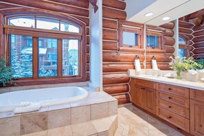 A log cabin bathroom with a large window, a bathtub, wooden cabinetry, and a sink area. - Villas At Tristant 201 (Mountain Village)
