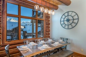 A dining area with a wooden table set for four, a large wall clock, and a window with a view of mountains. - Villas At Tristant 201 (Mountain Village)