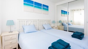 Quarto de hotel com duas camas, um espelho grande e obras de arte retratando uma cena de praia.