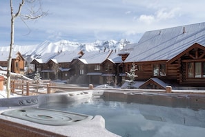 A wooden lodge with a hot tub in front, surrounded by snow-covered mountains. - Villas At Tristant 221 (Mountain Village)