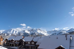 A row of wooden cabins with snow-covered roofs, set against a backdrop of snow-capped mountains under a clear blue sky. - Villas At Tristant 221 (Mountain Village)