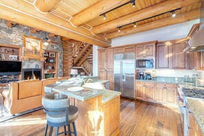 A spacious kitchen with wooden cabinets, a central island, and a stone fireplace. - Villas At Tristant 221 (Mountain Village)