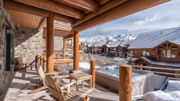 Una terraza de madera con sillas Adirondack y un jacuzzi, con vista a un paisaje montañoso nevado.