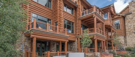 A log cabin with multiple balconies, stone walls, and a hot tub in the foreground.
