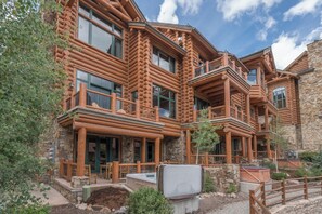 A log cabin with multiple balconies, stone walls, and a hot tub in the foreground. - Villas At Tristant 221 (Mountain Village)