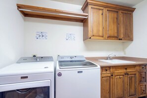 A laundry area with two white washing machines, a wooden cabinet, and a countertop with a sink. - Villas At Tristant 221 (Mountain Village)
