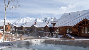 Una cabaña de madera con jacuzzi y montañas nevadas al fondo.