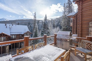 A wooden deck with a grill and seating, overlooking a snowy forest and mountains. - Villas At Tristant 221 (Mountain Village)