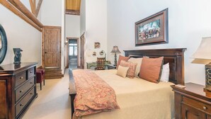 Un dormitorio con una cama grande, cabecera de madera, un escritorio con lámpara y un cuadro en la pared.