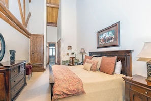 A bedroom with a large bed, wooden headboard, a desk with a lamp, and a painting on the wall. - Villas At Tristant 221 (Mountain Village)