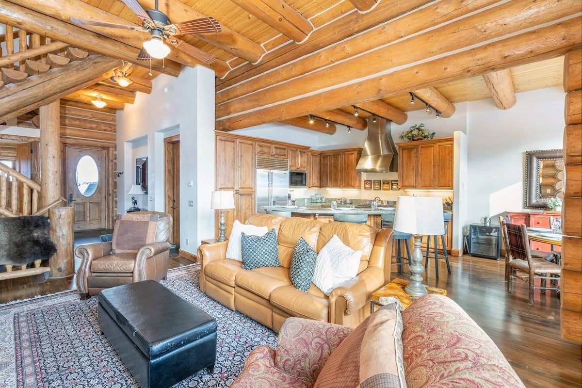 A spacious living area with a high ceiling, wooden beams, a leather sofa, and a patterned rug.