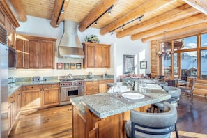 A spacious kitchen with wooden cabinets, granite countertops, and a large island with bar stools. - Villas At Tristant 221 (Mountain Village)