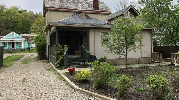 Ein einstöckiges Haus mit Veranda, Schornstein und einem kleinen Garten mit Blumentöpfen.