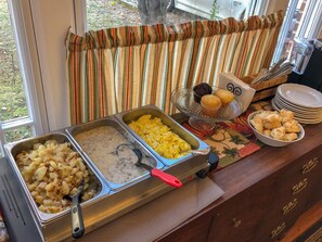 Un bufé con diversas opciones de comida, incluyendo papas, huevos revueltos y muffins.