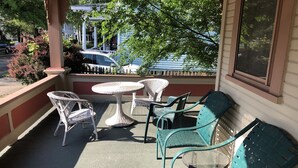 A covered outdoor seating area with wicker chairs and tables, a green sofa, and a view of parked cars and buildings in the background. - Primrose Path Bed and Breakfast Hocking Hills between Logan and Athens (Nelsonville)
