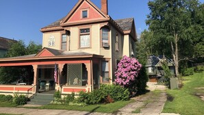 A two-story house with a porch, a small garden with pink flowers, and a sign indicating it is a B&B. - Primrose Path Bed and Breakfast Hocking Hills between Logan and Athens (Nelsonville)