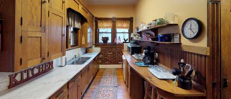 A kitchen with wooden cabinets, a marble countertop, a brick wall, and a clock on the wall.