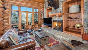 A log cabin interior with a stone fireplace, leather furniture, and a mounted bison head. - Villas At Tristant 127 (Mountain Village)