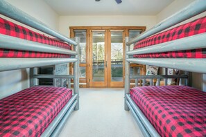 Een kamer met stapelbedden, een houten deur en uitzicht op bomen en bergen.