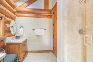 Un baño con vigas de madera, un lavabo con espejo y zona de ducha.