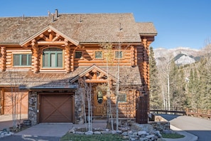 Une cabane en rondins avec un garage, une véranda et une vue sur les montagnes en arrière-plan.