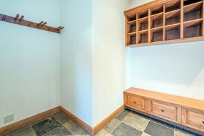 Un rincón de una habitación con un perchero, un armario de madera con estantes abiertos y un suelo de baldosas.