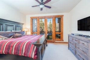 A bedroom with a bed, a dresser, a television, and a sliding glass door leading to a balcony.