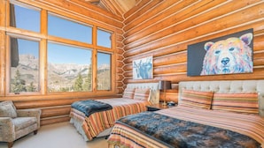 A log cabin bedroom with a large window, a bed, a chair, and a painting of a bear. - Villas At Tristant 127 (Mountain Village)