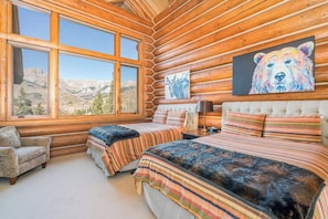 Une chambre située dans un chalet en rondins, avec une grande fenêtre, un lit, une chaise et un tableau représentant un ours.