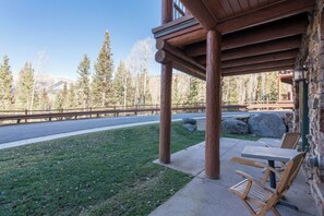 A wooden outdoor seating area with a stone wall and a view of a forested mountain range.
