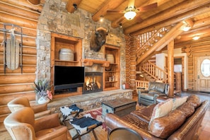 A log cabin interior with a stone fireplace, leather furniture, and a mounted buffalo head.