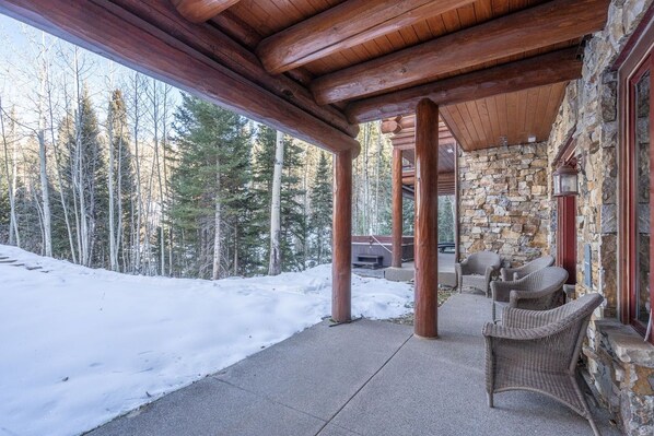 A covered outdoor area with stone walls, wooden beams, and wicker furniture.
