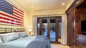 Ein Schlafzimmer mit einer großen amerikanischer Flagge, einem Bett mit gemusterten Kissen, einem Schminktisch und einer Schiebetür zu einem verschneiten Außenbereich.