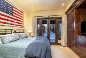 Une chambre à coucher avec un grand drapeau américain, un lit agrémenté d’oreillers à motifs, une commode et une porte-fenêtre coulissante donnant sur un espace extérieur enneigé.